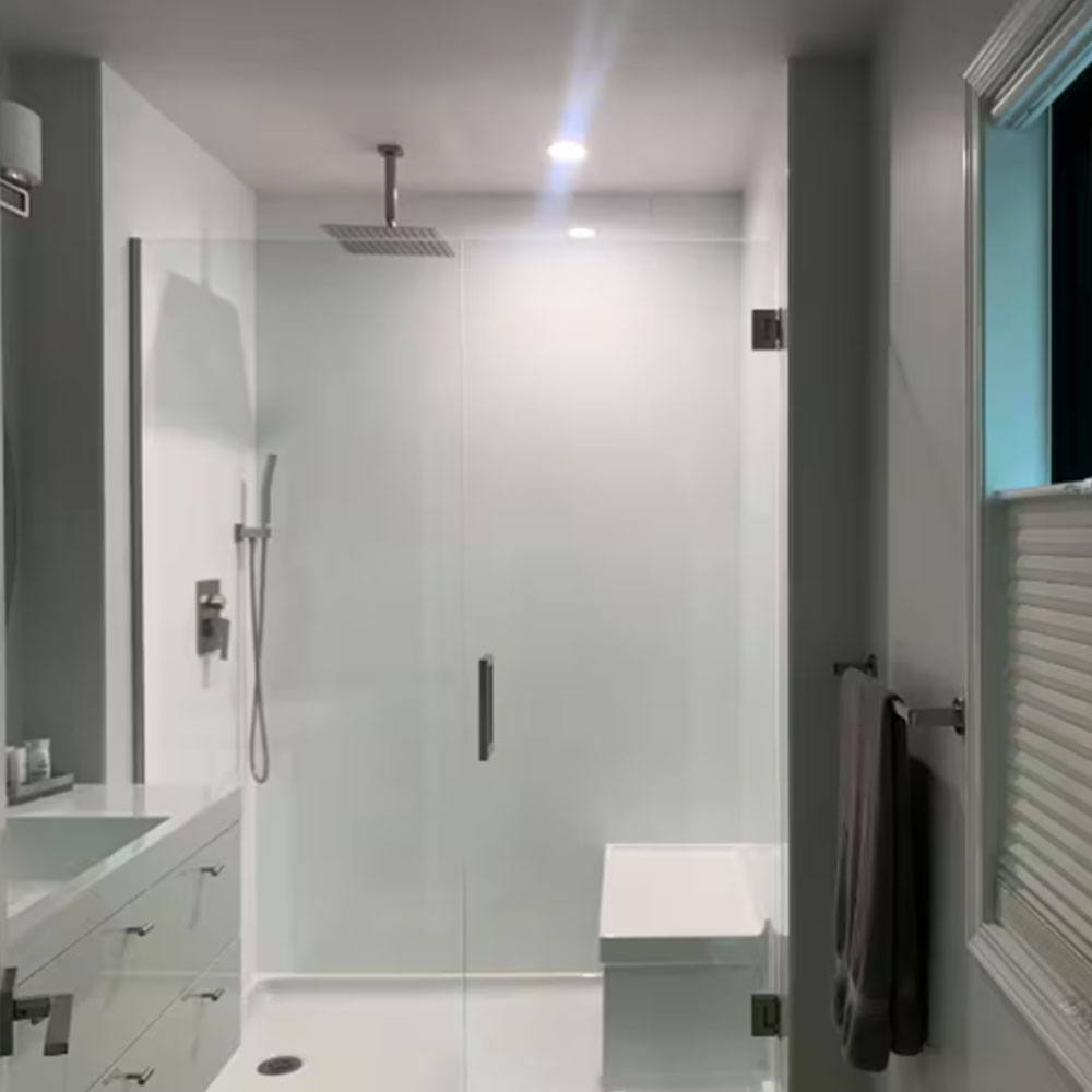 A modern, minimalistic bathroom with a glass-enclosed shower featuring a rain showerhead, a built-in white bench, white walls, a vanity with drawers on the left, and a towel hanging on the right wall.