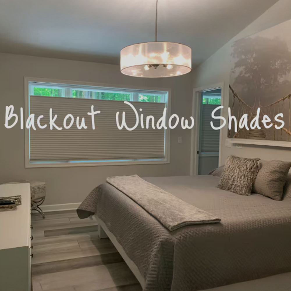 A modern bedroom with a large window covered by blackout shades, a bed with gray bedding, a white dresser, and a ceiling light fixture. The text "Blackout Window Shades" is overlaid on the image.